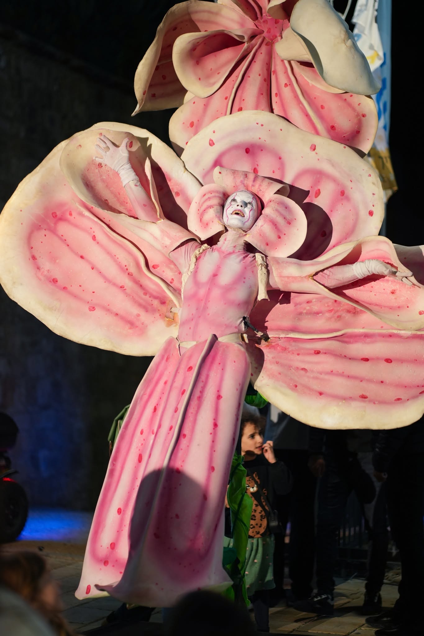 A large pink puppet character performs in the street.