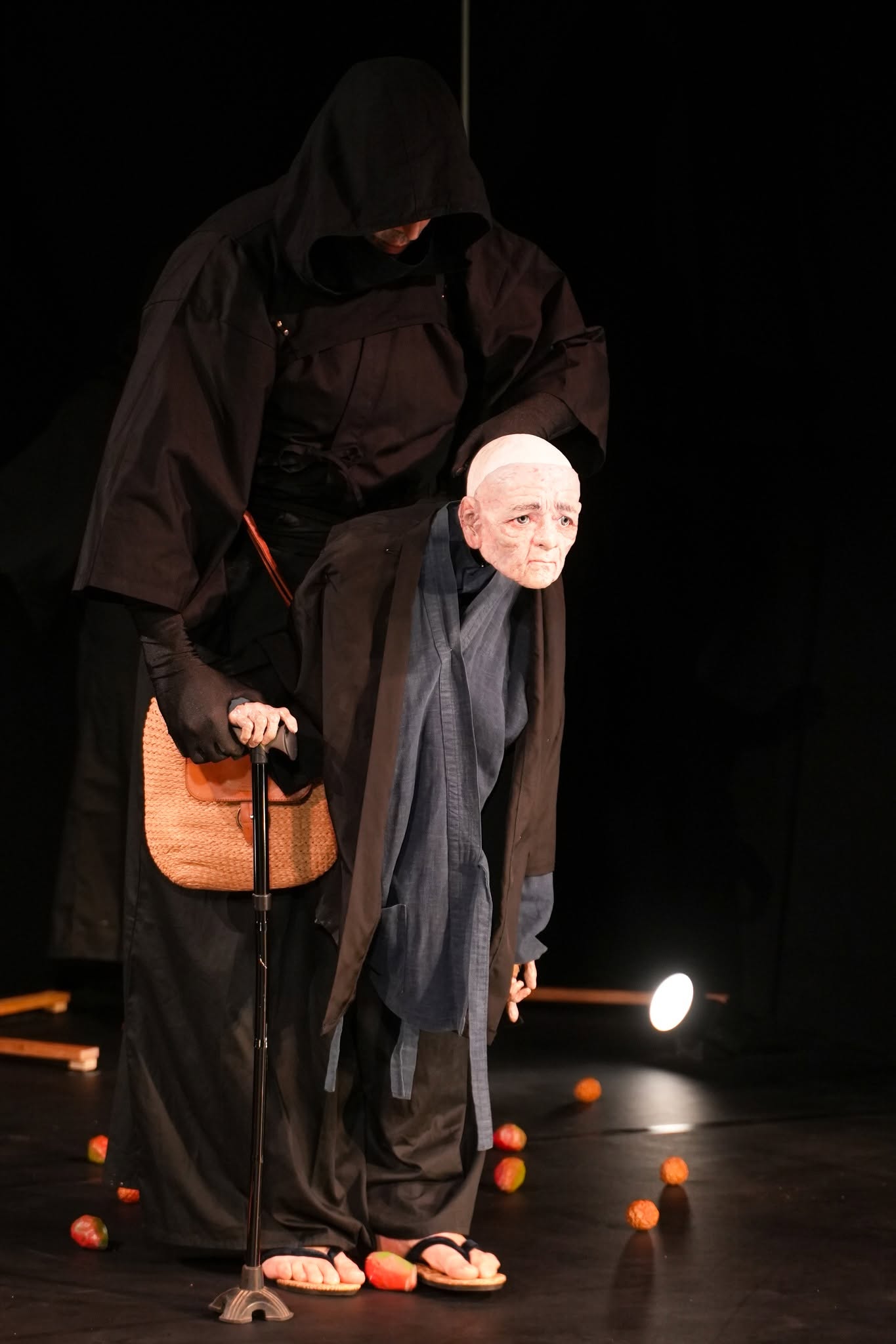An actor peers out from a tall black character on a dark stage.