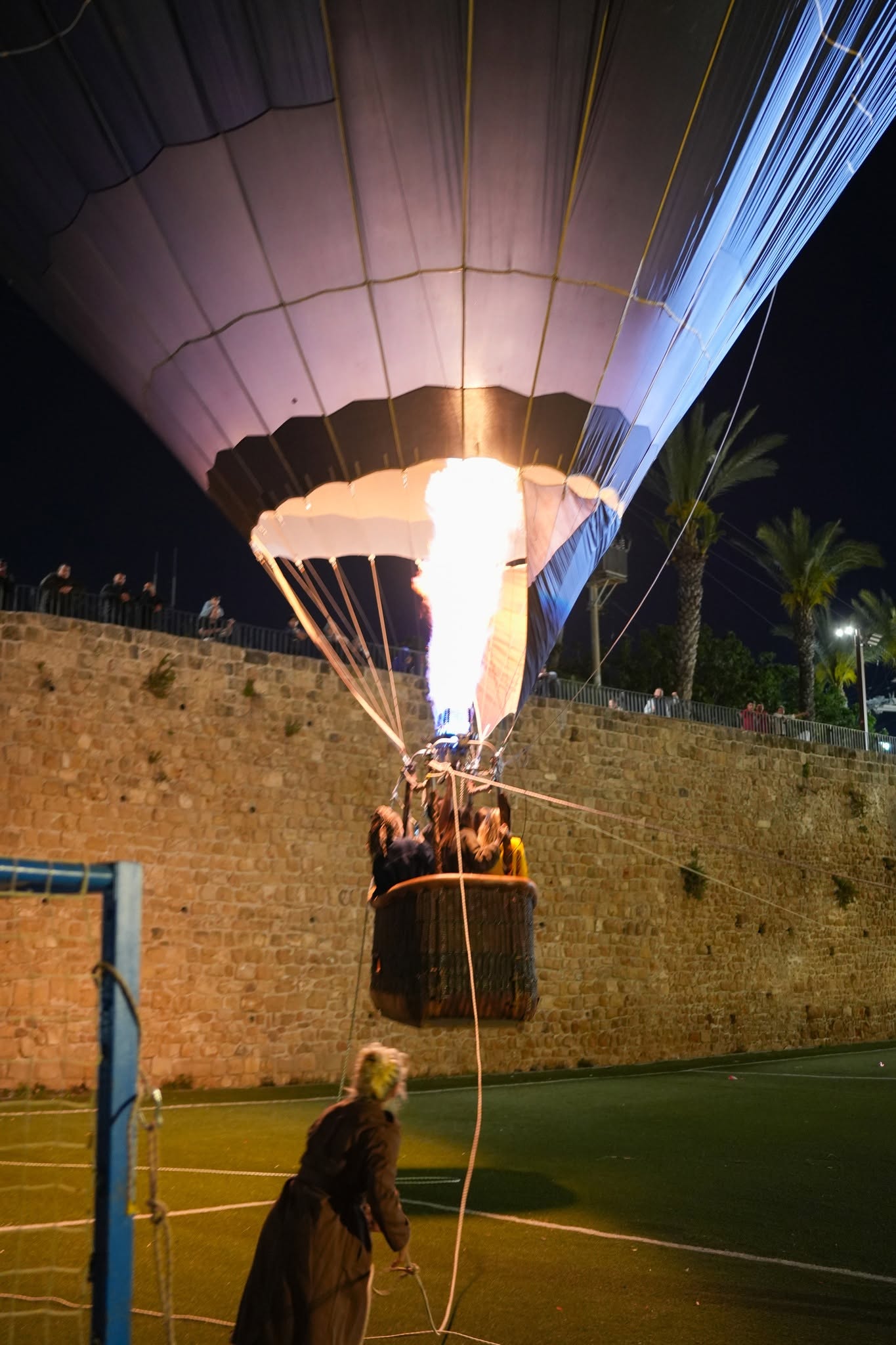 An illuminated hot-air balloon rises over a stone wall at night.