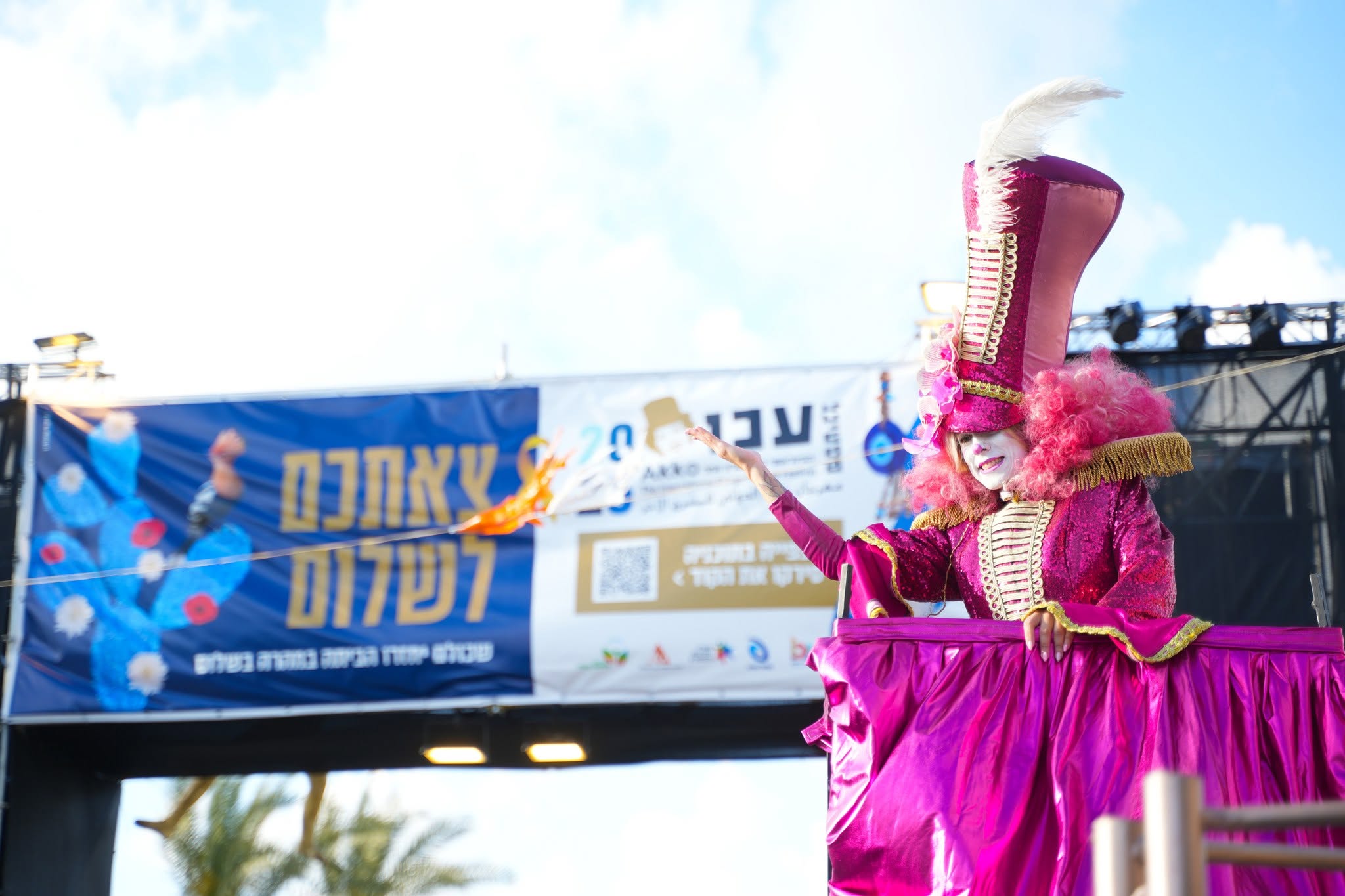 A tall pink stilt character performs near festival signage.
