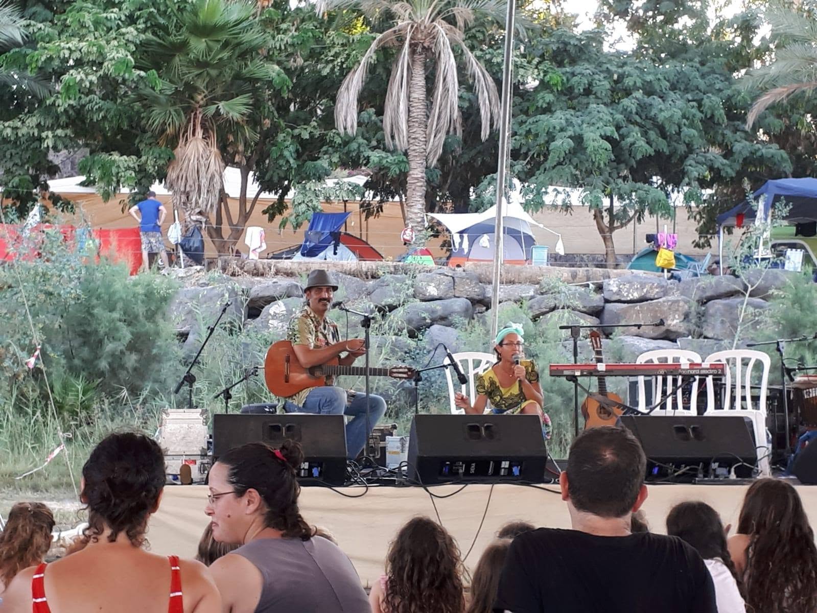 Musicians perform for families in a shaded area among trees.