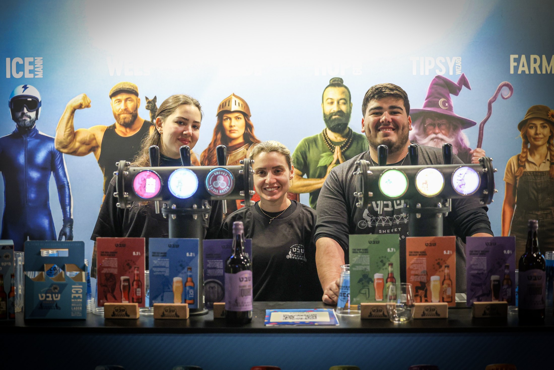 Three smiling exhibitors behind a stand of drinks and products.
