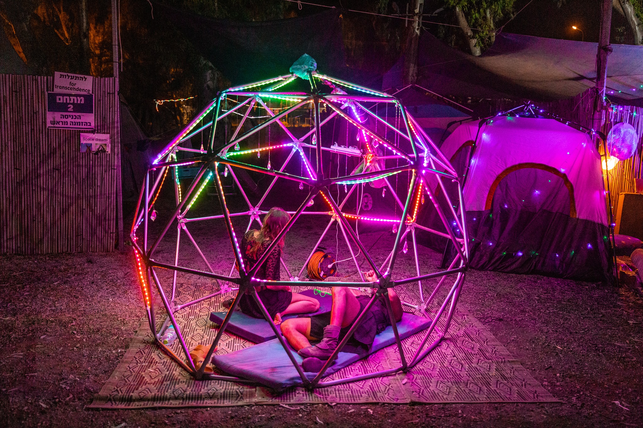 Two people sit inside a purple-lit geodesic dome.