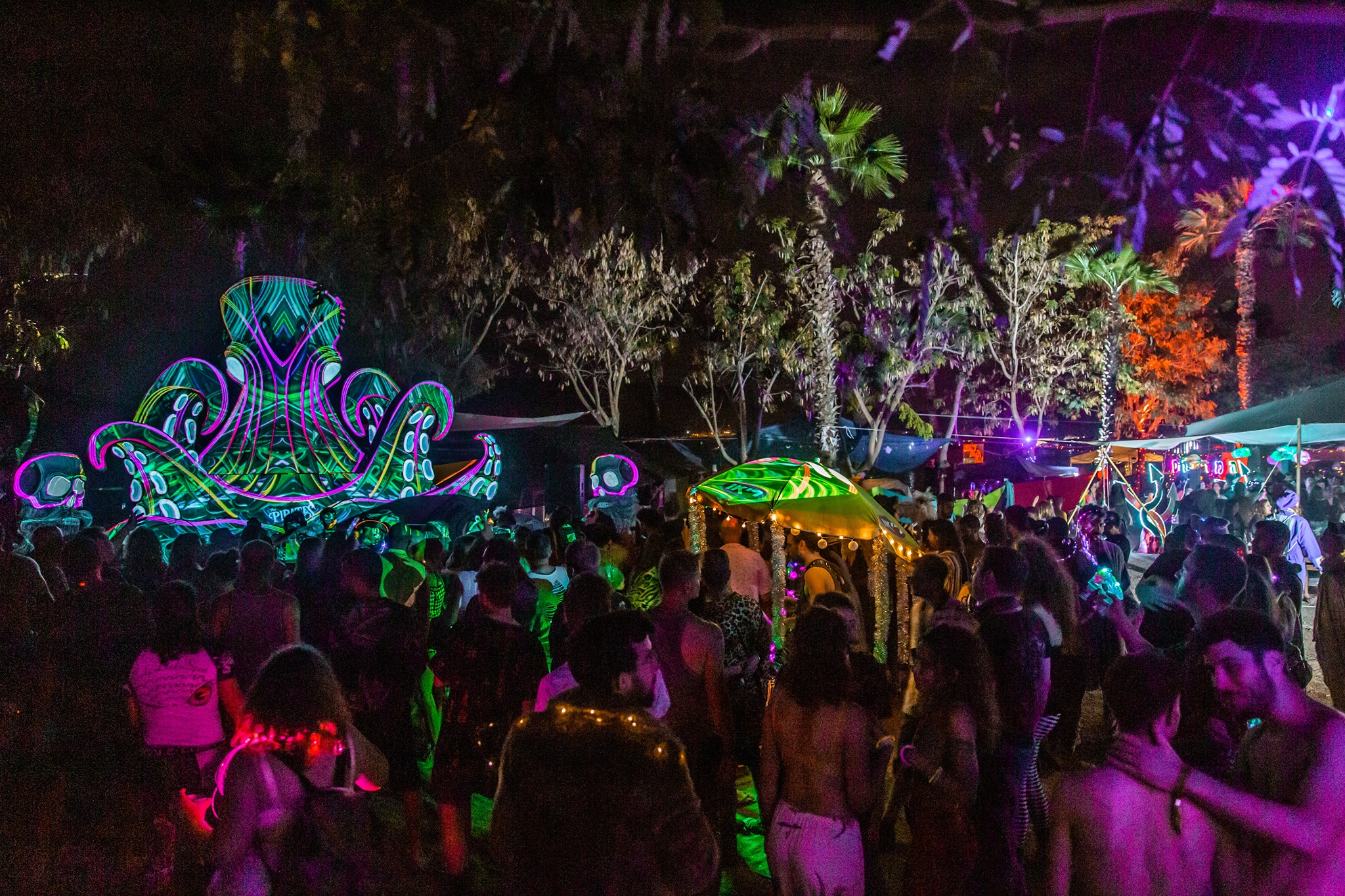 A night-time crowd dances among green and purple illuminated installations.