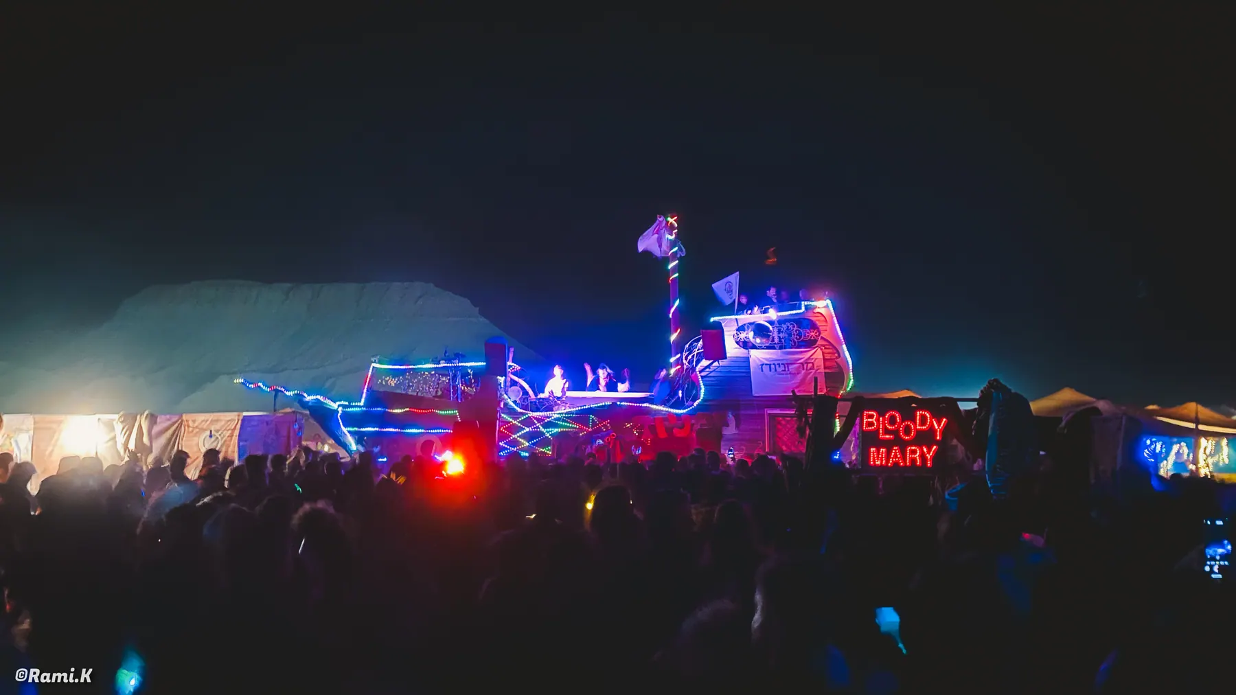 A crowd faces an illuminated art vehicle used as a night-time stage.