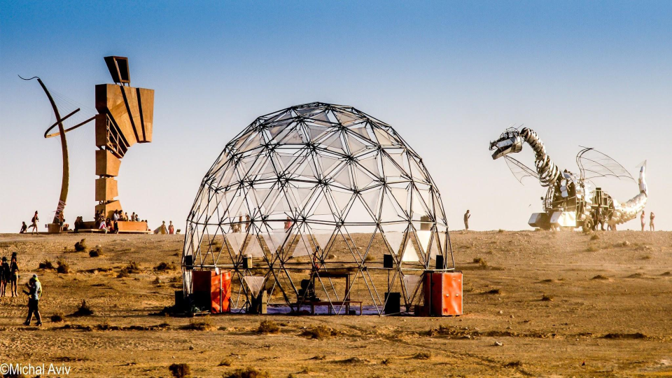 A geodesic dome, sculptures and people on the desert site.