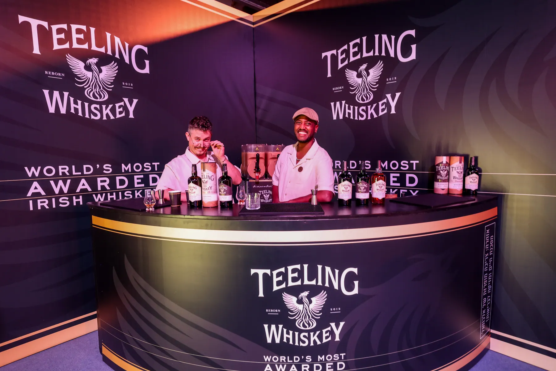 Two exhibitors stand behind a Teeling Whiskey counter.