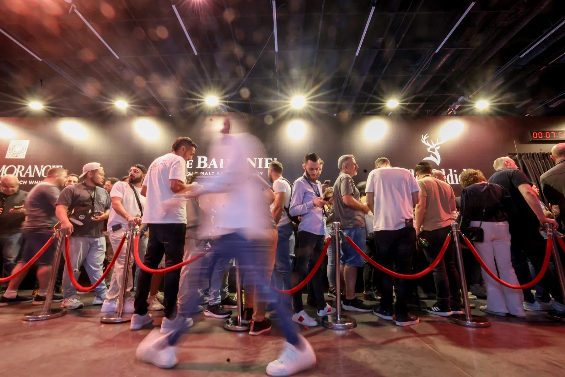 A line of visitors winds between stands under exhibition lighting.