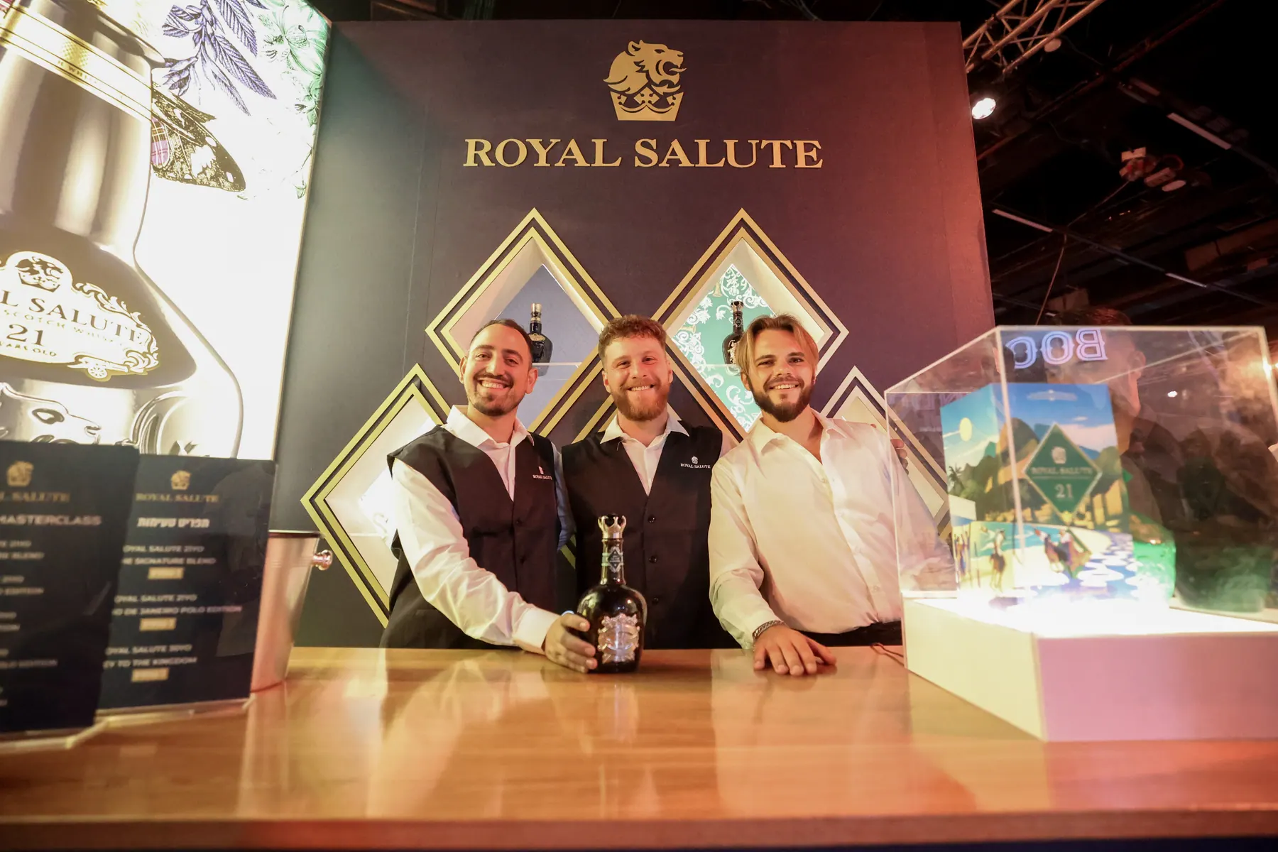 Three exhibitors stand behind a Royal Salute display.