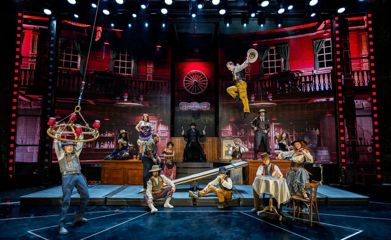 Group performance with dancers, drummers and acrobats on a red stage.